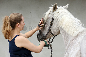 Bruchmuehle  Deutschland  junge Frau buerstet den Kopf ihres Pferdes