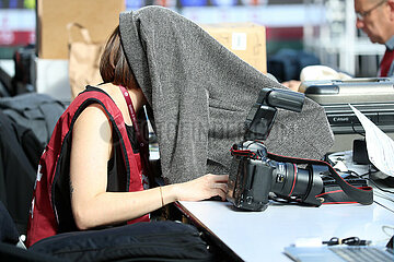 Paris  Frankreich  Pressefotografin arbeitet mit einer Jacke ueber dem Kopf an ihrem Laptop