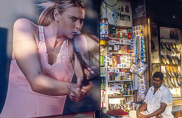 India. Mumbai (Bombay) Colaba district. Contrast in a pub poster with Russian tennis champion Maria Sharapova and an Indian shopkeeper