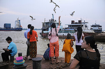 Yangon  Myanmar  Menschen stehen am Ufer des Yangon River und fuettern Moewen  mit Schiffen im Hintergrund
