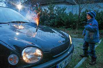 Kind beim Anzuenden eines Feuerwerkskoerper am Auto