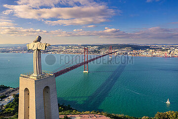 Portugal. Lisbon. Almada. Aerial view of Christ the King on the other side of the Tagus and the 25th of April Bridge. It is a national sanctuary of the Catholic Church and a religious monument representing the Sacred Heart of Jesus. The monument is 110m high and remains one of the tallest buildings in the country