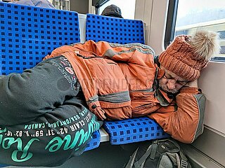 Obdachloser schlaeft in einem Zug