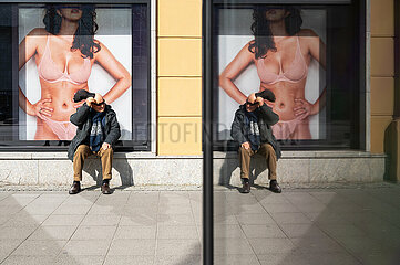 Berlin  Deutschland  Mann sitzt am Kurfuerstendamm vor einem Schaufenster und spiegelt sich in einer Vitrine