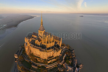 France. Normandy. Manche (50) Aerial view of Mont Saint Michel at sunrise seen from the southeast. In the foreground  the abbey dwellings  then the choir and the apse of the abbey church  in the flamboyant Gothic style  and finally the steeple of the church  in the Romanesque style. The construction of the monastery is spread over several centuries and mixes different styles. In the background on the right  the islet of Tombelaine