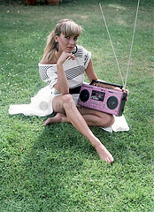 Berlin  Deutsche Demokratische Republik  junge Frau sitzt im Gras und hoert Musik aus einem Kassettenrecorder
