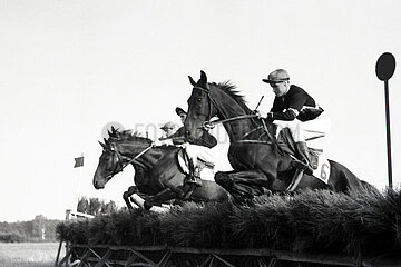 Hoppegarten  Pferde und Jockeys springen ueber eine Huerde. Schwarzer Adler mit Klaus Albrecht (links) und Garschak mit Wolfgang Thom