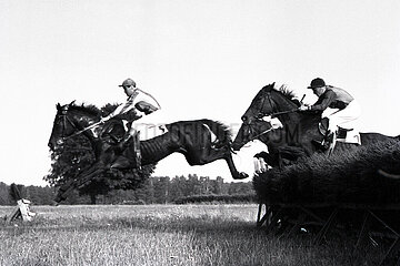 Hoppegarten  Pferde und Jockeys springen ueber eine Huerde. Wanderlilly mit Manfred Slowinski (links) und Ostland mit H. Keppke