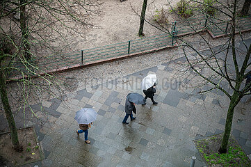 Berlin  Deutschland  Personen mit Schirmen geht waehrend Aprilwetter im Regen auf nassem Gehweg entlang