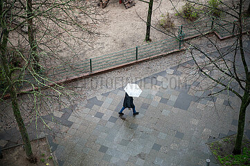 Berlin  Deutschland  Person mit Schirm geht waehrend Aprilwetter im Regen auf nassem Gehweg entlang