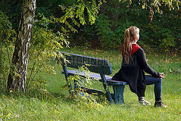 Seewalde  Deutschland  Frau sitzt allein auf einer Parkbank und meditiert