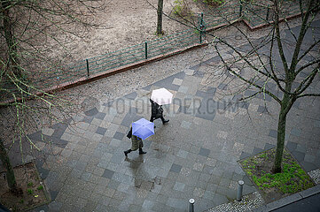 Berlin  Deutschland  Personen mit Schirmen gehen waehrend Aprilwetter im Regen auf nassem Gehweg entlang