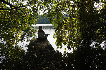 Seewalde  Deutschland  Silhouette: Frau sitzt allein auf einem Steg an einem See und meditiert