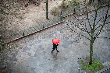 Berlin  Deutschland  Person mit Schirm geht waehrend Aprilwetter im Regen auf nassem Gehweg entlang