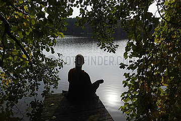 Seewalde  Deutschland  Silhouette: Frau sitzt allein auf einem Steg an einem See und meditiert