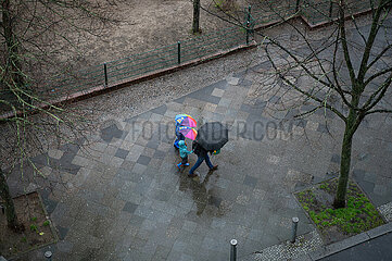 Berlin  Deutschland  Personen mit Schirmen gehen waehrend Aprilwetter im Regen auf nassem Gehweg entlang