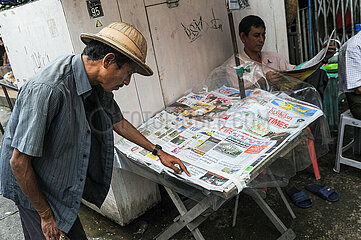 Yangon  Myanmar  Zeitungsverkaeufer liest an seinem Zeitungsstand in der Zeitung