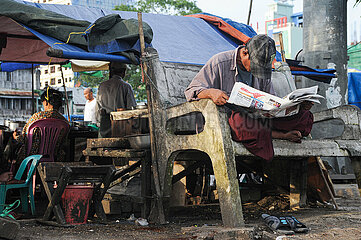 Yangon  Myanmar  Ein Mann sitzt auf einer Bank am Ufer des Yangon River und liest Zeitung
