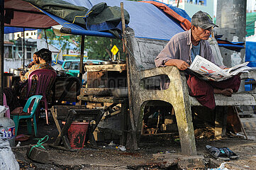 Yangon  Myanmar  Ein Mann sitzt auf einer Bank am Ufer des Yangon River und liest Zeitung
