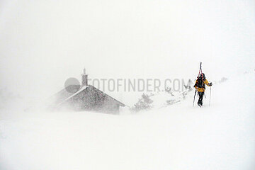 Krippenbrunn  Oesterreich  Skifahrer laeuft bei heftigem Schneefall durch den Tiefschnee eine Piste hinauf