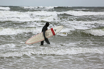 Binz  Deutschland  Mann laeuft mit seinem Surfbrett durch die Wellen der stuermischen Ostsee