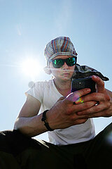Wolgast  Deutschland  junger Mann mit Kopftuch und Sonnenbrille schaut auf sein Smartphone