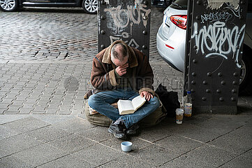 Berlin  Deutschland  Ein wohnungsloser Mann sitzt am Strassenrand und liest ein Buch