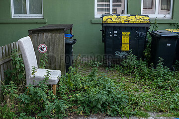 Deutschland  Bremen - Muelleimer vor einem Wohnhaus  davor ein wild entsorgter Stuhl