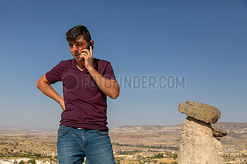 Tuerkei  Ortahisar - Tuerke telefoniert mit handy  Goereme-Nationalpark in Kappadokien  mit im Bild Tuffsteine