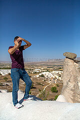 Tuerkei  Ortahisar - Tuerke telefoniert mit handy  Goereme-Nationalpark in Kappadokien  mit im Bild Tuffsteine
