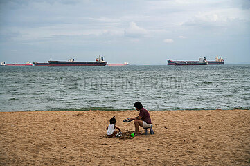 Singapur  Republik Singapur  Frau mit Kind am Strand des East Coast Park und Containerschiffe auf dem Wasser