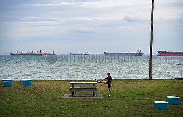 Singapur  Republik Singapur  Frau treibt am Ufer des East Coast Park Sport  dahinter Containerschiffe auf dem Wasser