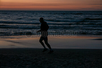 Polen  Kolobrzeg - Mann joggt am Strand an der Ostsee bei Sonnenuntergang
