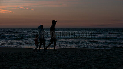 Polen  Kolobrzeg - junge Familie spaziert am Strand an der Ostsee bei Sonnenuntergang