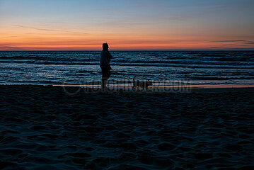 Polen  Kolobrzeg - Aeltere Frau mit Hund am Strand an der Ostsee bei Sonnenuntergang
