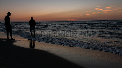 Polen  Kolobrzeg - junge Manner geniessen Sonnenuntergang an der Ostsee