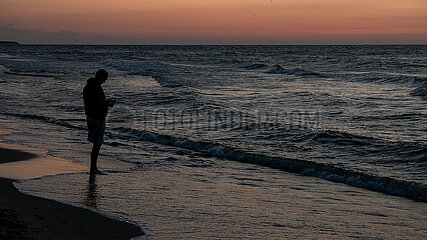 Polen  Kolobrzeg - Sonnenuntergang an der Ostsee  Mann checkt handy