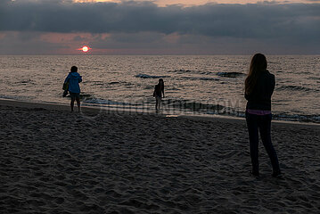 Polen  Kolobrzeg - Touristinnen geniessen den Sonnenuntergang am Ostseestrand