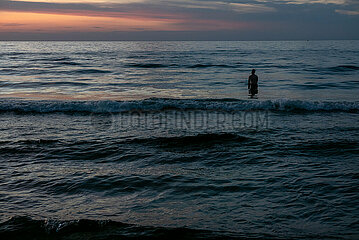 Polen  Kolobrzeg - Sillhouette eines im Wasser stehenden Urlaubers an der Ostseekueste bei Sonnenuntergang
