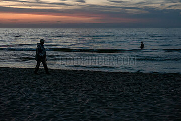 Polen  Kolobrzeg - Sillhouetten von Urlaubern an der Ostseekueste  Mann steht im Wasser bei Sonnenuntergang