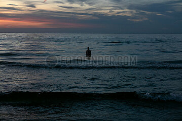 Polen  Kolobrzeg - Sillhouette eines im Wasser stehenden Urlaubers an der Ostseekueste bei Sonnenuntergang