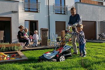 Polen  Wrzesnia - Vater und Sohn beim Rasenmaehen im Garten ihres Reihenhauses  Mutter mit Geschwistern im Hintergrund