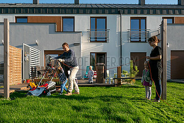 Polen  Wrzesnia - Vater und Sohn beim Rasenmaehen im Garten ihres Reihenhauses  Mutter mit Tochter haelt Kabel