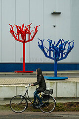Deutschland  Bremen - Fahrradfahrerin vor zwei trostlosen Plastikbaeumen an der Einfahrt zu einer Autowaesche-Anlage