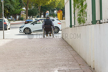 man in wheelchair seen from the back trying to cross a crosswalk