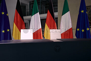 Berlin  Deutschland - Konferenztisch und zwei Stuehle vor den Fahnen Italiens Deutschlands und der EU.