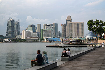 Singapur  Republik Singapur  Menschen sitzen an der Uferpromenade in Marina Bay mit der Skyline der Innenstadt