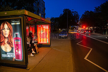 Polen  Poznan - Mit Werbeplakaten beleuchtete Bushaltestelle  Vater mit seinen Toechtern