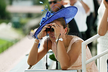 Iffezheim  Deutschland  junge Frau mit Hut schaut beim Pferderennen durch ihr Fernglas