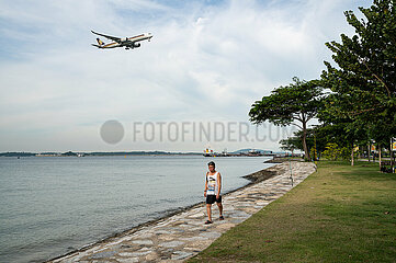 Singapur  Republik Singapur  Mann am Ufer des Changi Beach Park und einem Flugzeug im Landeanflug im Hintergrund